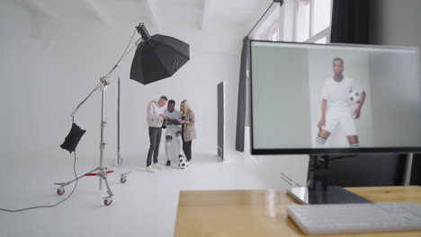 Monitor-with-an-advertising-cover-of-the-picture-On-the-background-a-photographer-a-football-player-a-model-and-a-director-look-at-photos-from-a-photo-shoot-for-the-cover-on-a-camera